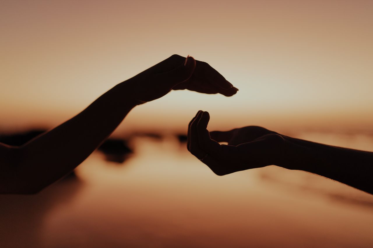 services-01 Silhouette of two hands reaching out at sunset, symbolizing connection and support.