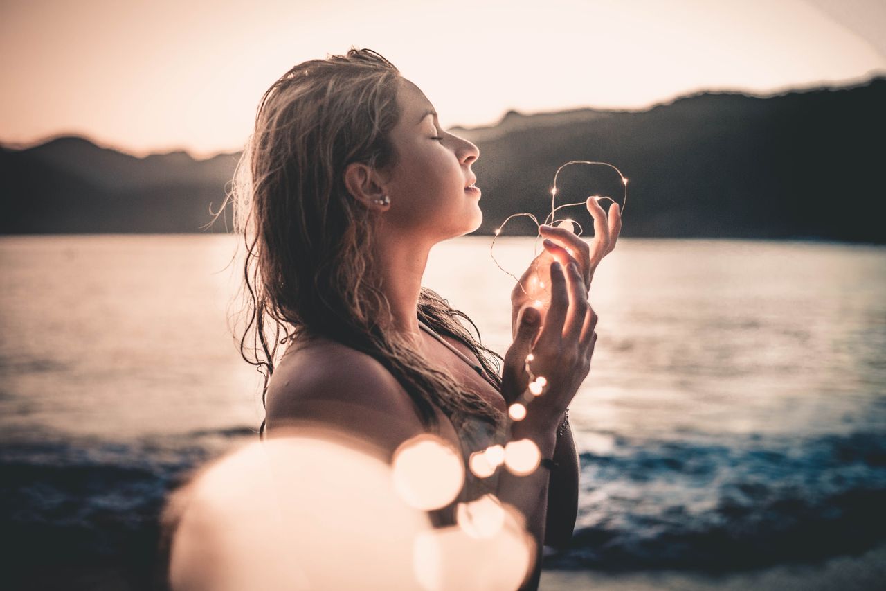 services-01 A woman enjoys a serene sunset on a beach in Ubatuba, Brazil holding glowing lights.